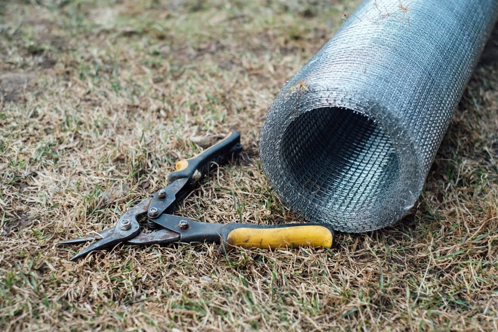 There are garden shears and a roll of metal mesh on the grass.