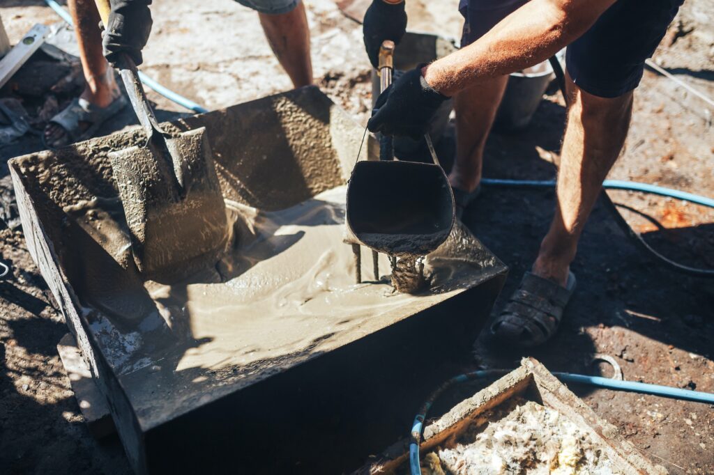 Workers work with cement mortar, loading the hopper bucket with mortar with a shovel